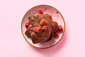 Plate with pieces of raspberry chocolate brownie on pink background