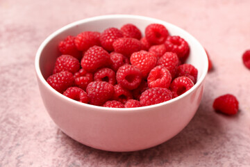 Bowl with fresh raspberries on pink background