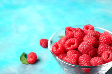 Glass bowl with fresh raspberries on blue background