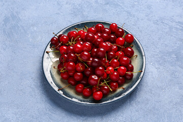 Plate with red sweet cherries on blue background