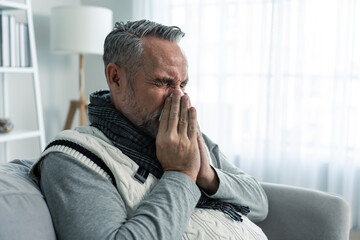 Caucasian senior man having running nose and sneezing in living room. 