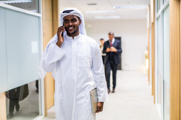 Arab Businessman using smartphone while standing in corridor of office. 