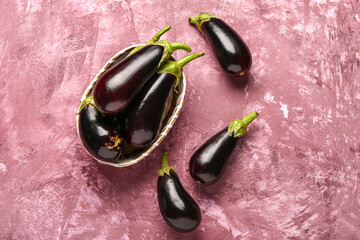 Wicker basket with fresh eggplants on pink background