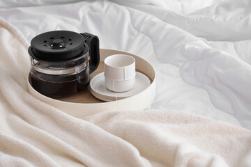 Fototapeta na wymiar Messy bed with white blanket and coffee on tray, closeup