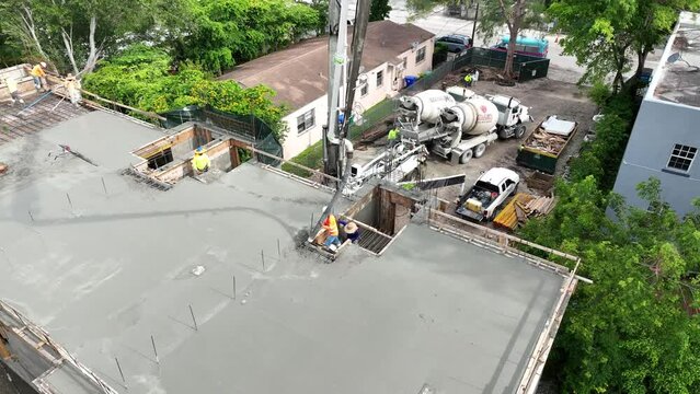 Two construction workers finishing pouring concrete on first part of floor surface and moving towards staircase. Drone view of foundation laying on building site