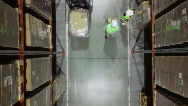 Top View: Warehouse Workers in Special Uniforms Efficiently Navigate the Rows of Shelves Filled with Goods in the Logistic Centre, Focused on their Tasks