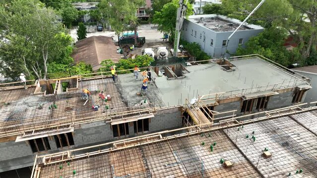 View from drone on foremen spreading and leveling first layer of freshly poured concrete on steel reinforcement bar. Construction site of new motels