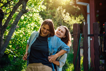 Two happy laughing lesbian women are having fun in a green garden in the rays of the bright sun....