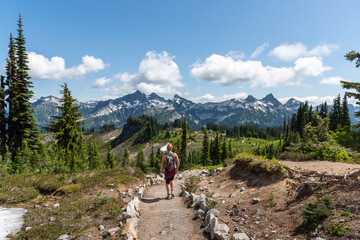 Fototapeta na wymiar Woman hiking on trail through beautiful majestic mountains landscape in the stunning Mt. Rainier National Park, Pacific Northwest, Washington State