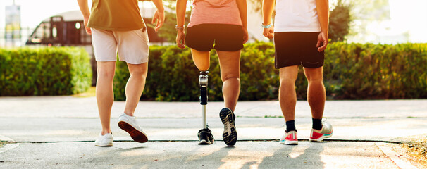 Friend support Friend with a prosthetic leg while exercising outdoor. People walking together on park outdoor. Exercise walking  woman with prosthetic leg and friend support together in  park outdoor