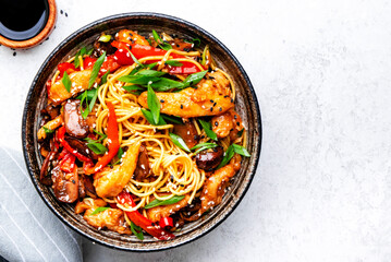 Stir fry noodles with chicken slices, red paprika, mushrooms, chives, soy sauce and sesame seeds in ceramic bowl. Asian cuisine dish. White table background, top view