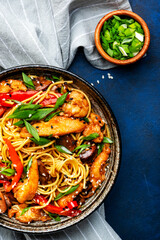 Stir fry egg noodles with chicken, paprika, mushrooms, chives and sesame seeds in ceramic bowl. Asian cuisine dish. Blue stone table background, top view