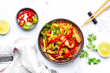 Asian cuisine stir fried chicken breast, red paprika and zucchini with sesame seeds, lime and soy sauce in ceramic bowl. White table background, top view