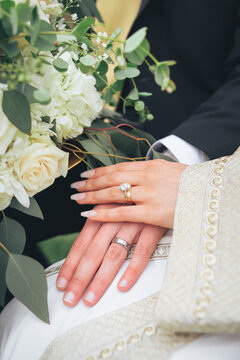 Bride and groom hands with diamond wedding rings, gold jewelry, and white floral bouquet &ndash; close-up detail of marriage ceremony, romance, engagement, eternal love, happiness, cultural wedding traditio