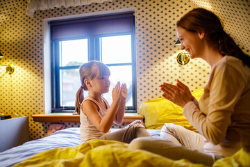 Young girl playing the clapping game with her mother in the bedroom