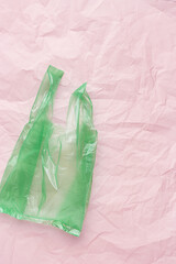 Plastic free concept, top view one green crumpled plastic bag on pink wrinkled background. Disposable polythene packet. Eco trend minimal style vertical photo, Biodegradable packaging waste.