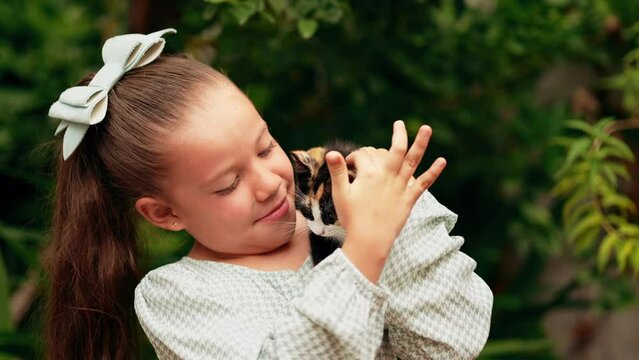 Niña linda latina rubia contenta y sonriente acariciando jugando con mascota un pequeño gatito gato felino travieso e inquieto y curioso en el jardín al exterior al aire libre un día lluvioso 