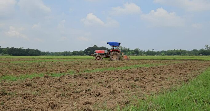 Defocused view of Unidentified farmer with tractor preparing land for sowing with tractor and cultivator, Odisha, India