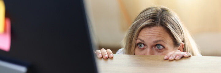 Scared and shocked woman in panic behind desk looking at computer screen.