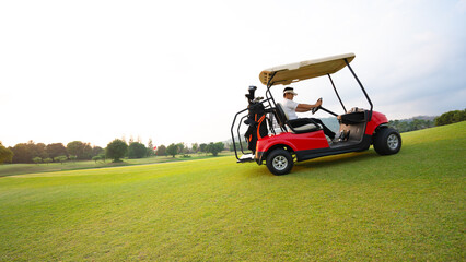 Fototapeta premium Side view of golfers riding golf cart on golf course with green grass at warm sunny day.