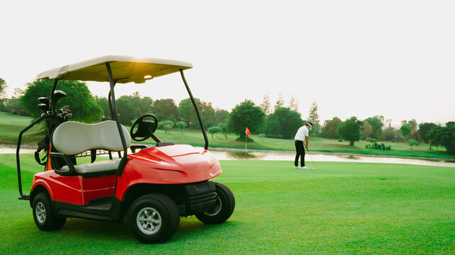 Red golf cart on golf course with green grass and golfer is putter golf in background.