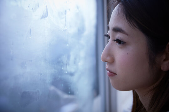 窓際で暗い表情をして外を見る女性