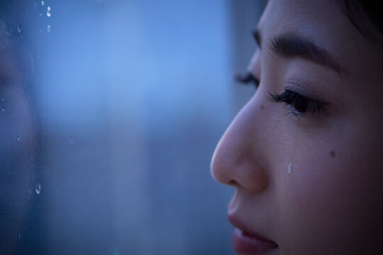 窓際で涙を流す女性のアップ