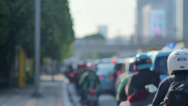 A blur image of Jakarta's urban traffic density dominated by motorcycles with a sidewalk on the side. Depicts high pollution, heat, congestion, fatigue from work, boredom, and inequality.