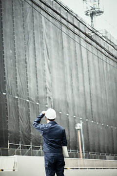 工事中の建物を見ている作業服とヘルメットの男性