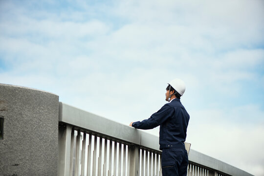 遠くを見ている橋の上の作業服の男性