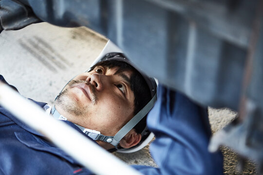 車の下に潜り込み作業をする作業服とヘルメットの男性