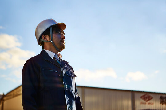 遠くを見ている作業服とヘルメットの男性