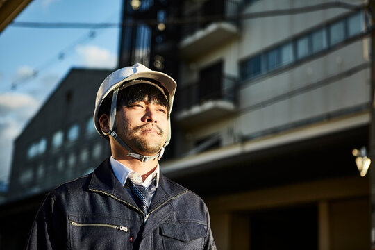 遠くを見ている作業服とヘルメットの男性