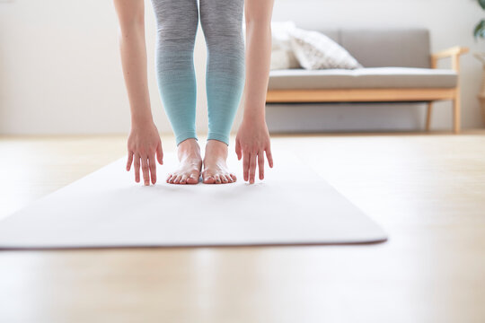 ヨガマットの上で前屈で床に手を付く女性の手元