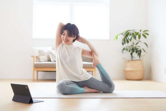 室内の床でノートパソコンを見ながらヨガのポーズをとる女性