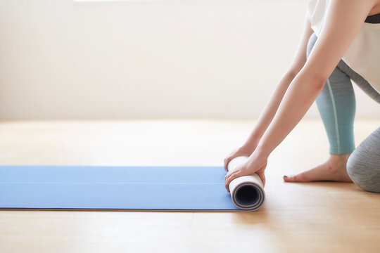 床でヨガマットを丸めている女性の手元