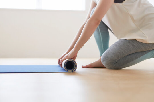 床でヨガマットを丸めている女性の手元