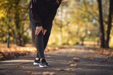 Low section of woman feeling knee injury during jogging in the park - obrazy, fototapety, plakaty