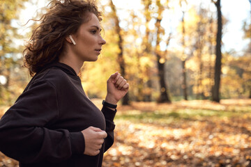 Mid shot of caucasian woman jogging in the park in the autumn   and wearing earphones - Powered by Adobe