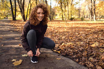 Woman in sports clothes tying shoes with fun before jogging in the park - Powered by Adobe