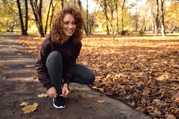 Zelfklevend Fotobehang Woman in sports clothes tying shoes with fun before jogging in the park © gpointstudio