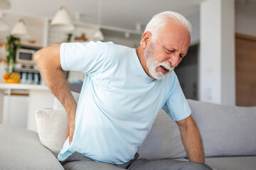 Senior man, with back pain, touches his back, illustrating sciatica and sedentary lifestyle....