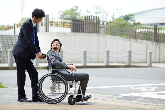 車椅子の男性を押しているスーツの男性