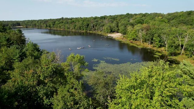 Drone flyover summer trees to pond with canoes shot in pocono mountains
