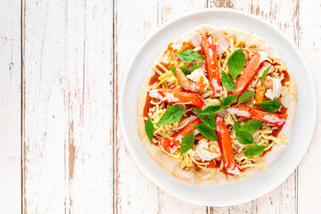 raw pizza with tomato sauce, shrimp, crab stick, sausage, sweet basil, oregano, mozzarella, cheddar, gouda, romano cheese in white ceramic plate on white wood texture background, top view, flat lay