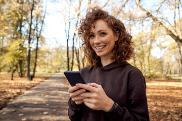Caucasian woman browsing mobile phone and looking away in the autumn park