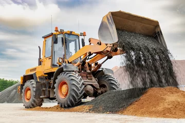 Fotobehang Powerful wheel loader or bulldozer isolated on sky background. Loader pours crushed stone or gravel from the bucket. Powerful modern equipment for earthworks and bulk handling. © Anoo