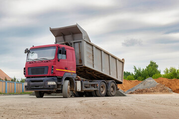 Dump truck with a raised body at a construction site. Transportation and unloading of sand or soil. Technique for transportation of bulk materials. Transportation of bulk building materials. © Anoo