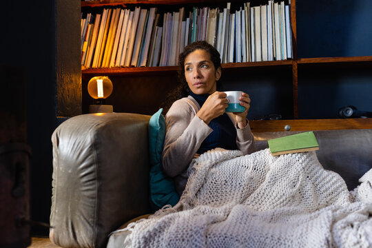 Biracial woman sitting on sofa, holding mug in living room