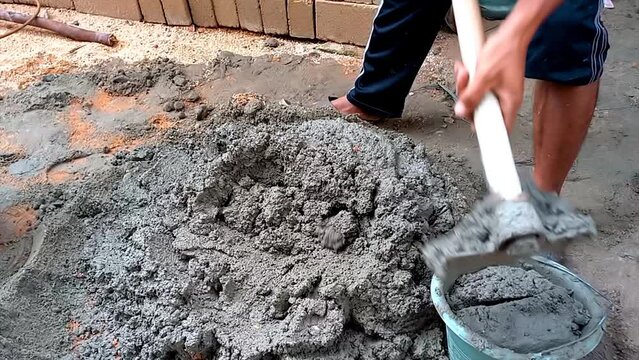 A Man Who Is Putting Cement Mixture Into A Black Bucket